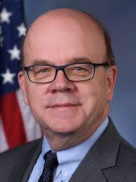 Official portrait of Jim McGovern (D-MA) wearing a dark suit and tie, in front of the American flag